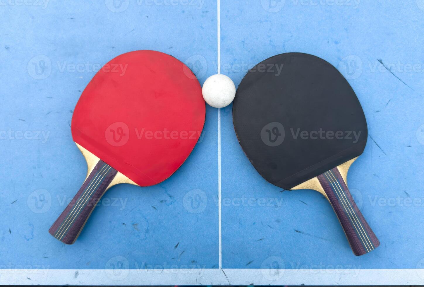 Red and black rackets for table tennis with white ball on blue background. Ping pong sports equipment in minimal style. Flat lay, top view, copy space photo