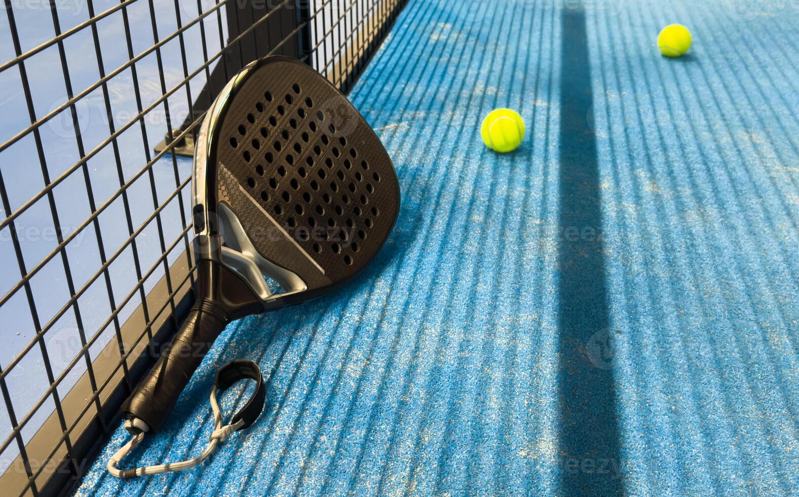 Padel racket and yellow ball behind net on a green court grass turf outdoors at sunset. Paddle is a racquet game. Professional sport concept with space for text photo