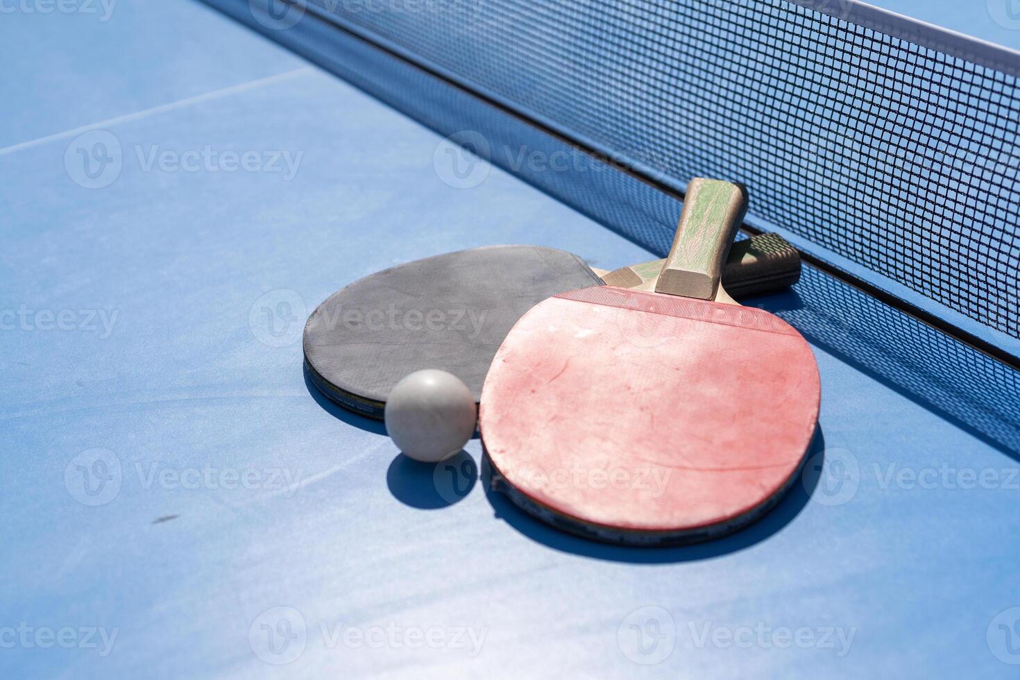 Two table tennis or ping pong rackets and ball on blue table with net photo