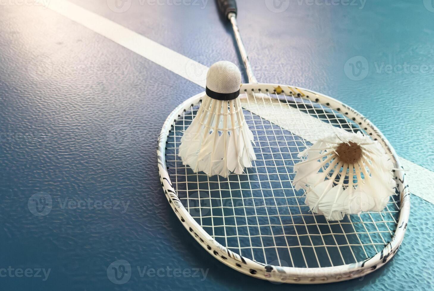 Cream white badminton shuttlecock and racket with neon light shading on floor in indoor badminton court, copy space, soft and selective focus. photo