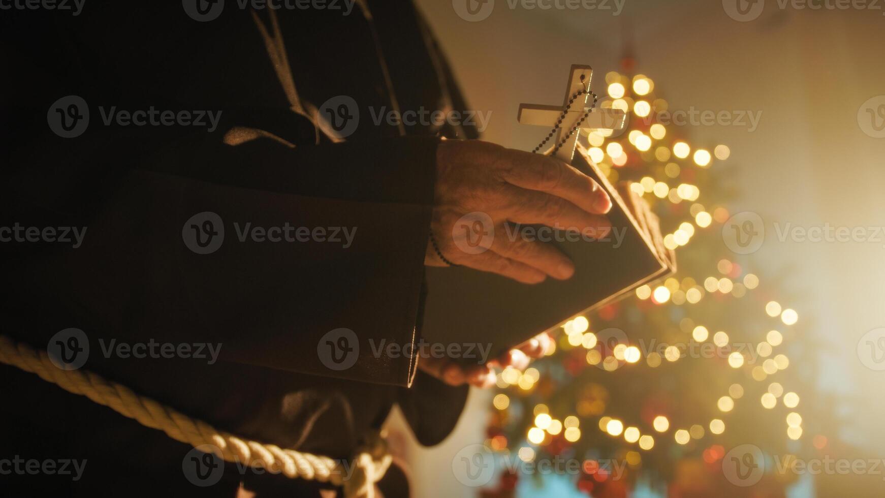 Priest Prays For A Peaceful Christmas On Christian Bible Book In Front Of Tree photo