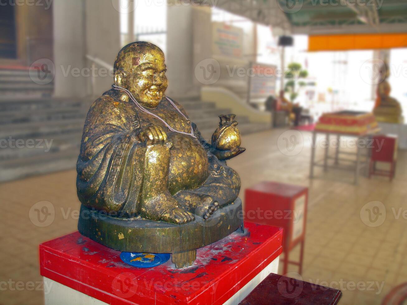 statue of smiling Buddha envelop by gold leaf in a Thai temple photo