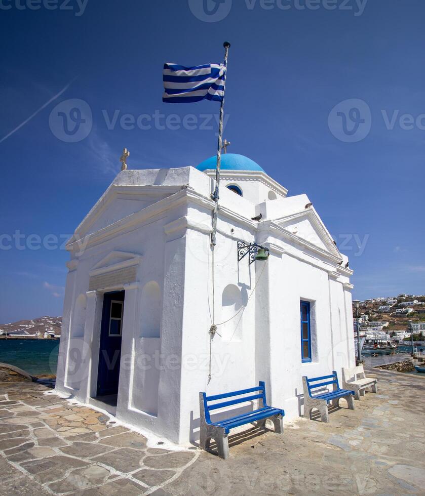 Whitewashed church in the harbor with Greece flag, Mykonos, Cyclades, Greece photo