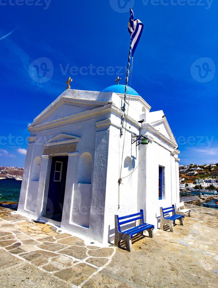 Whitewashed church in the harbor with Greece flag, Mykonos, Cyclades, Greece photo