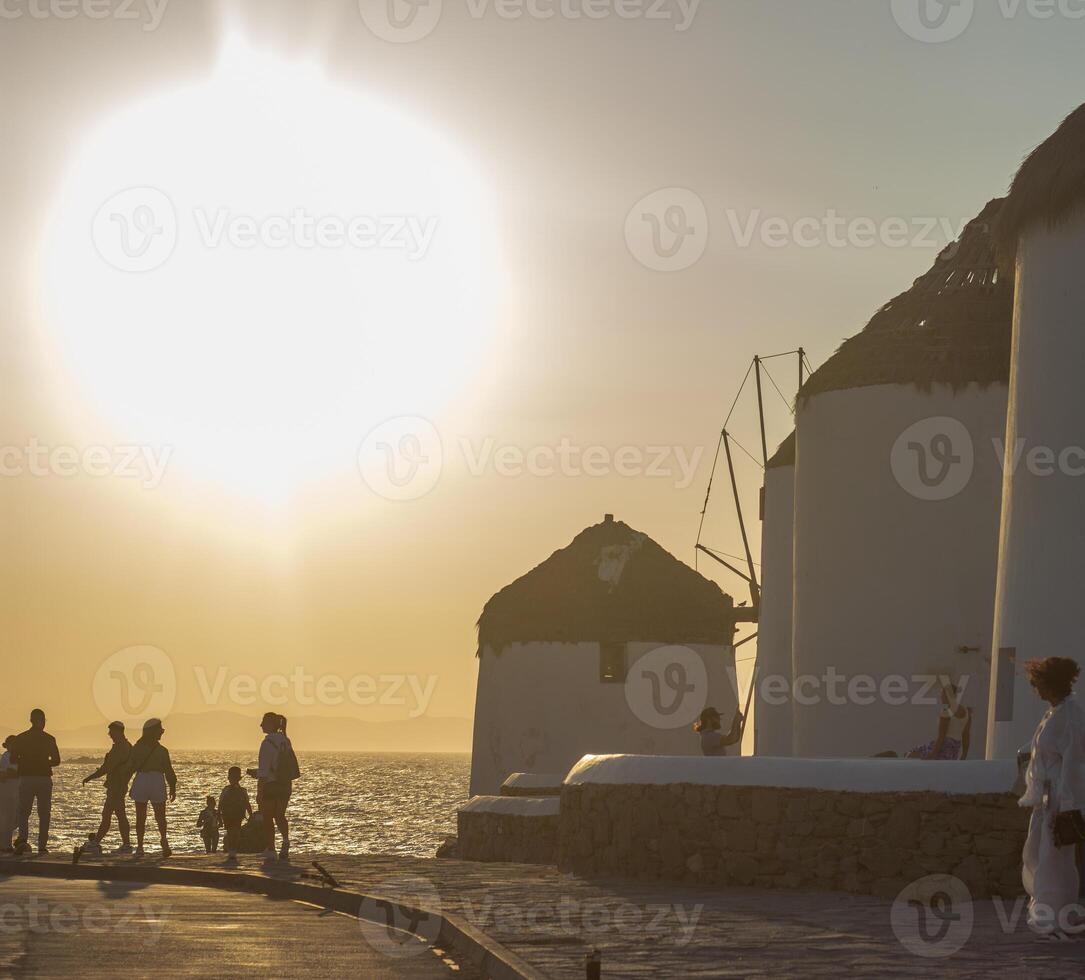 Traditional windmills with white walls and wooden structures at sunset in Mykonos, Greece. Historical architecture and travel concept. photo