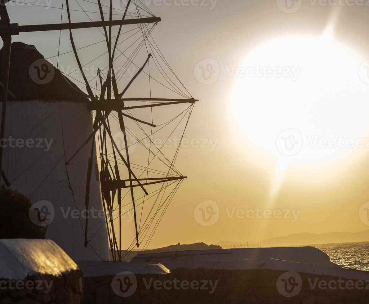 Traditional windmills with white walls and wooden structures at sunset in Mykonos, Greece. Historical architecture and travel concept. photo