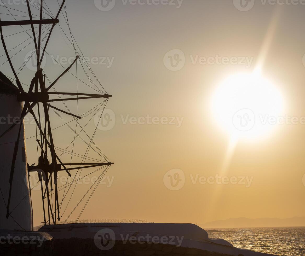 Traditional windmills with white walls and wooden structures at sunset in Mykonos, Greece. Historical architecture and travel concept. photo