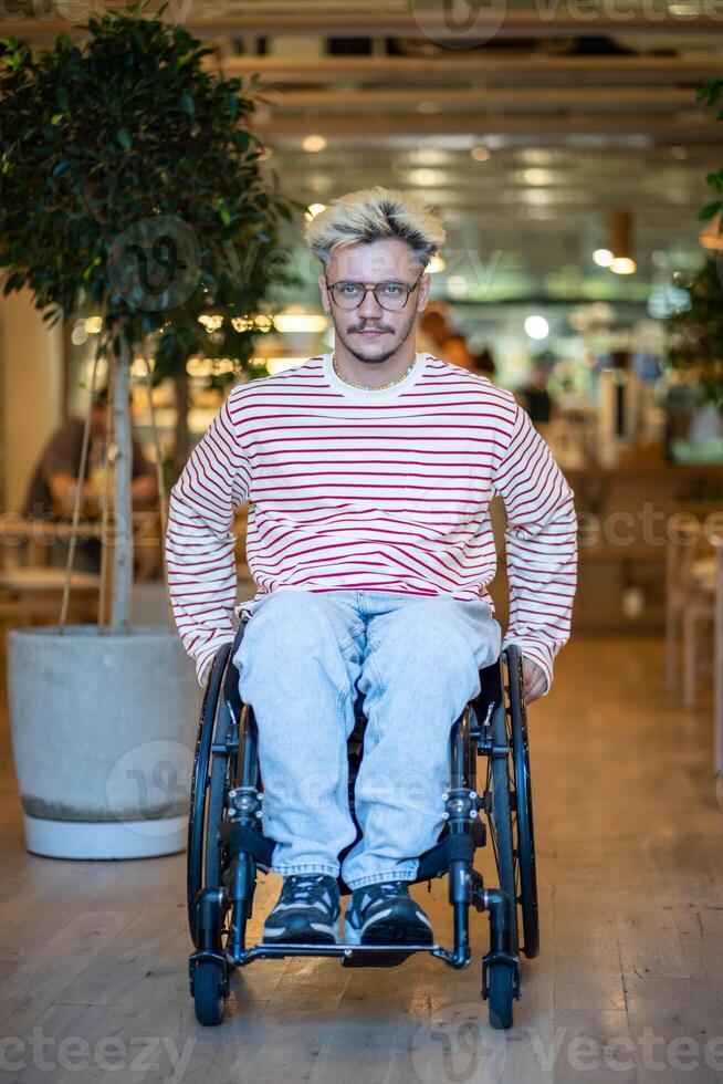 Confident disabled young man on wheelchair in cafe with adaptive accessible place for handicapped. photo