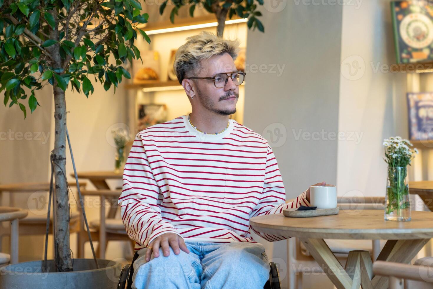 Thoughtful serene disabled man in wheelchair enjoys coffee in cafe alone at table. Coffee lover photo