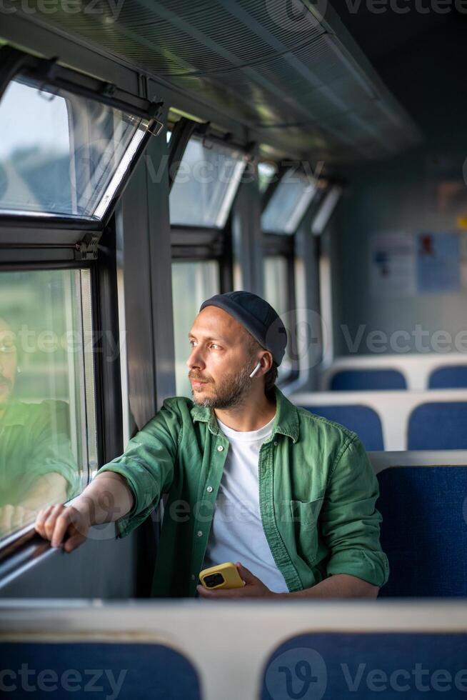 Interested tourist man travel by electric train looking at window enjoy trip with music in earphones photo