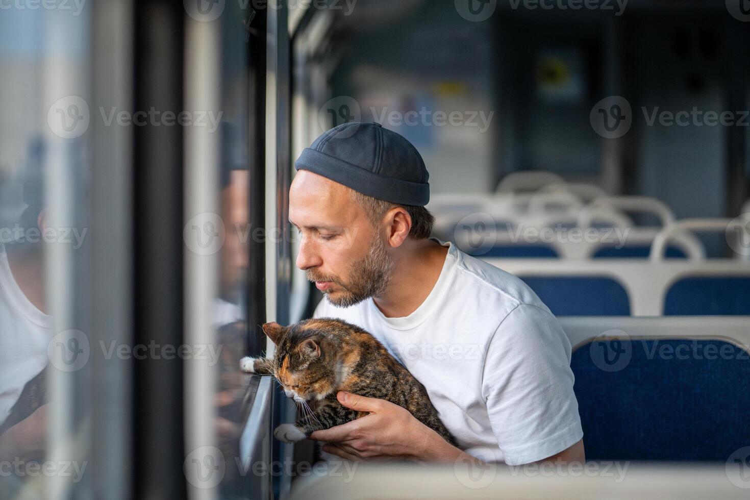 Attentive caring man pet owner traveling with fluffy cat in hands showing window in electric train. photo