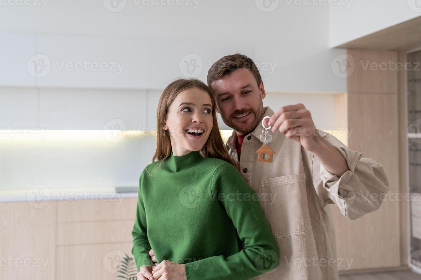 Moving house of young family. Excited couple embracing, celebrating with keys after relocation photo