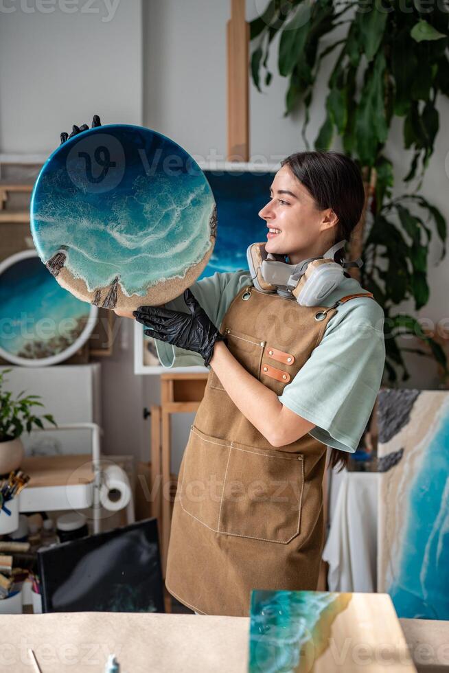 Smiling woman artist demonstrates finished painting made of epoxy resin. Liquid art technique. photo