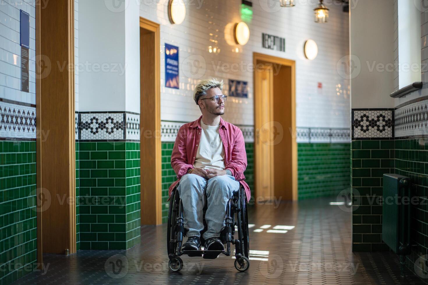 Thoughtful man student in wheelchair pauses in hallway near university classroom looking at window. photo