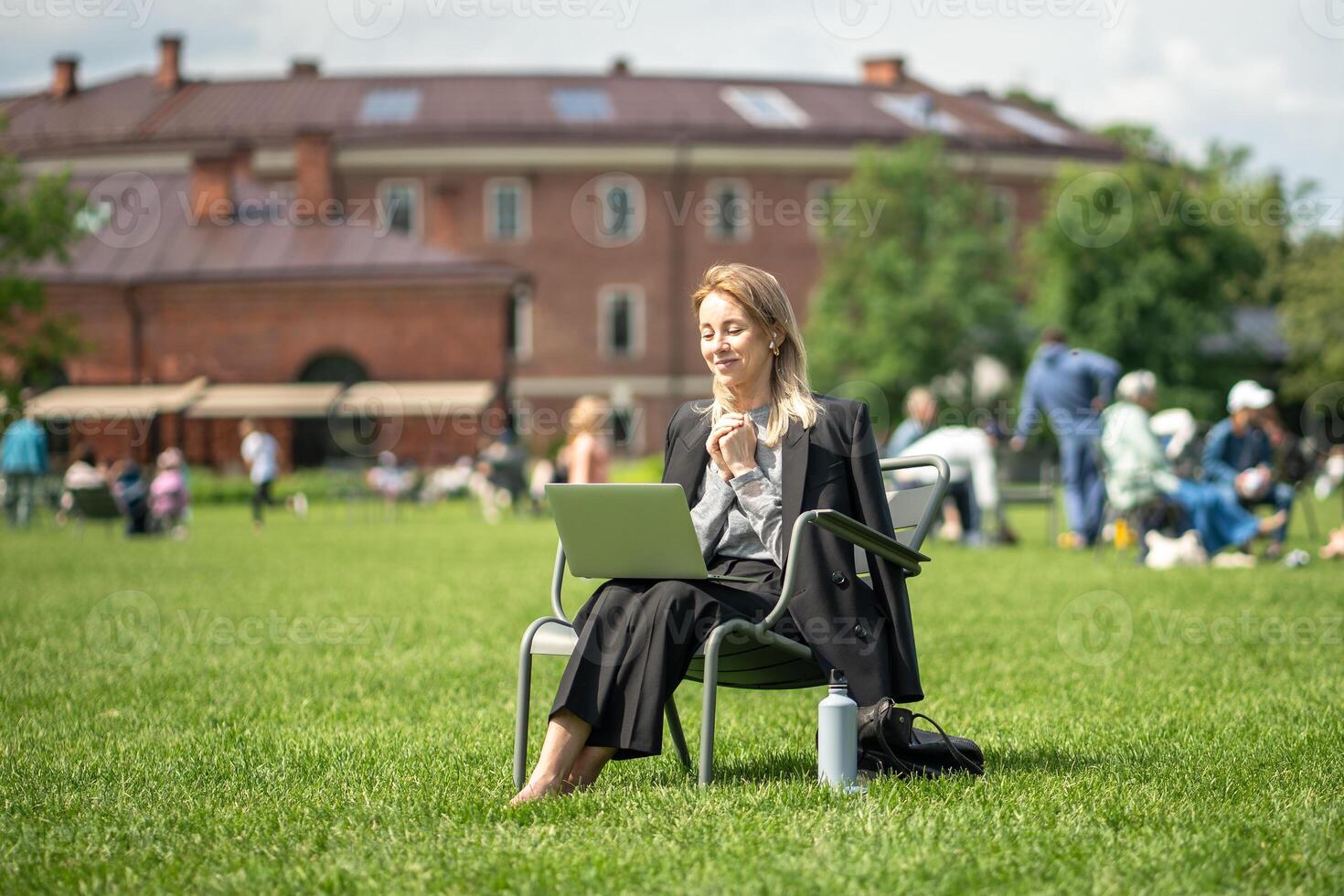 Confident businesswoman works on laptop with thermos in park in summer. call, outdoor work photo