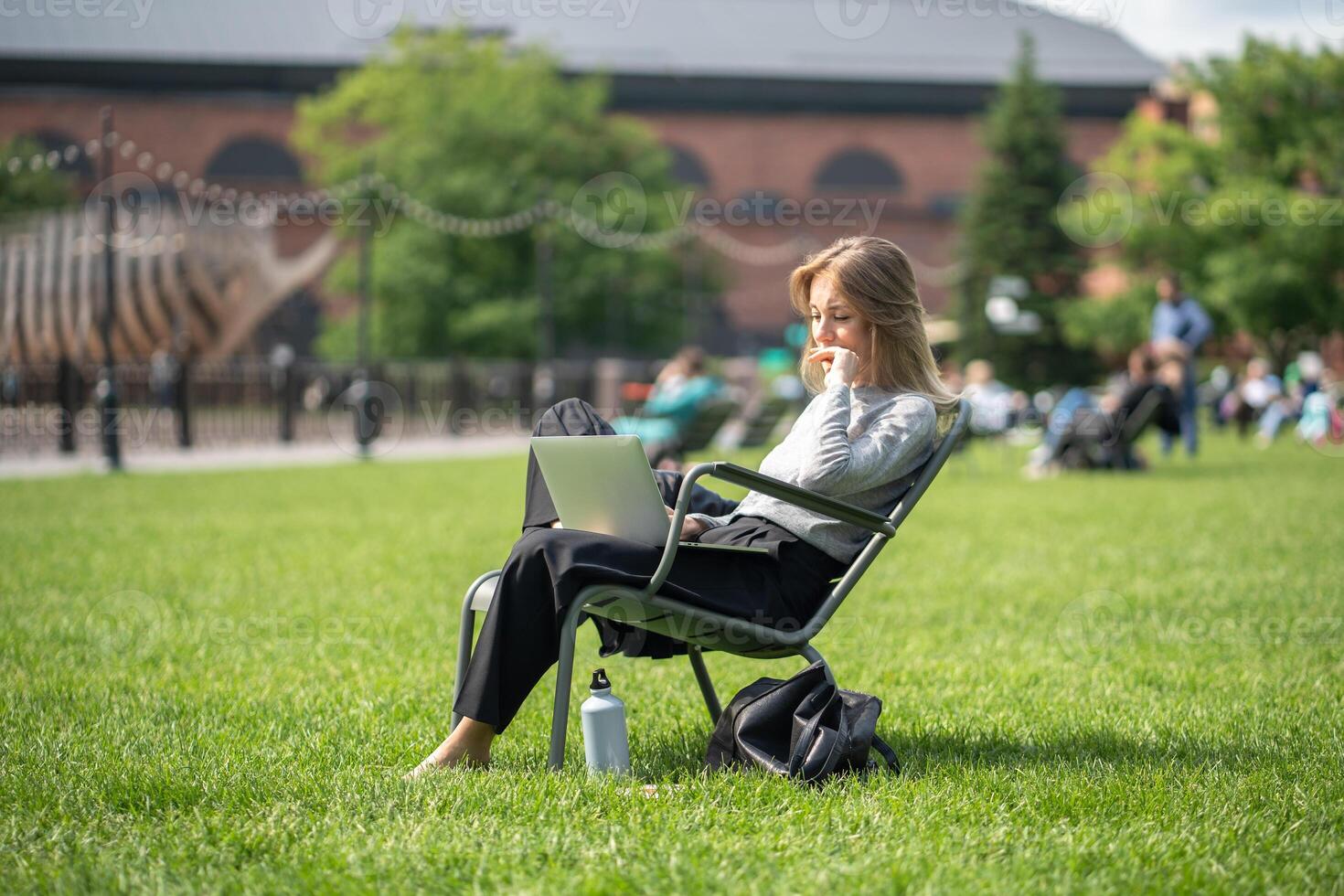 Content woman in park with laptop and insulated drink container, handling calls, watching series photo