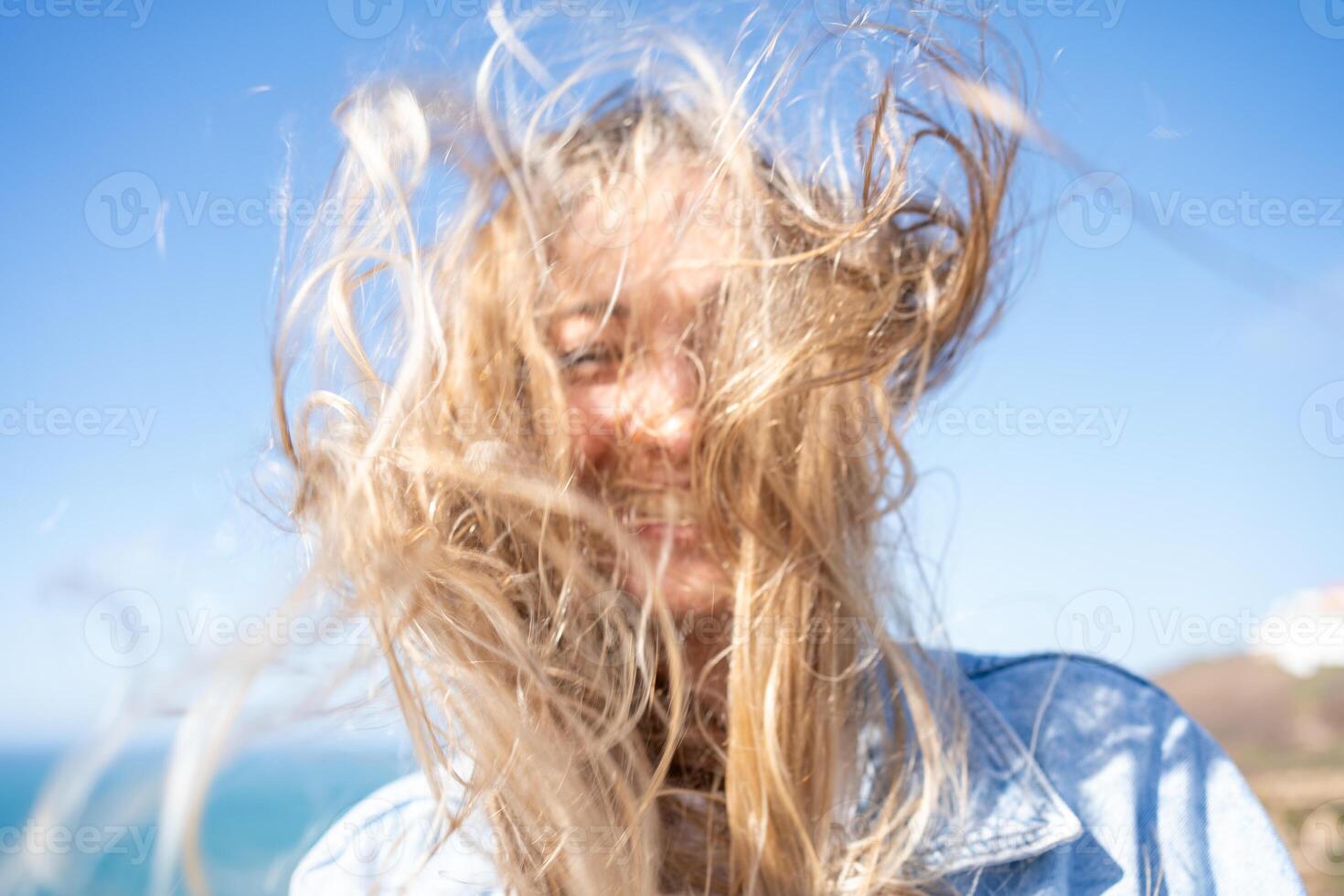 Happy woman with tousled messy long blond hair against clear blue sky photo