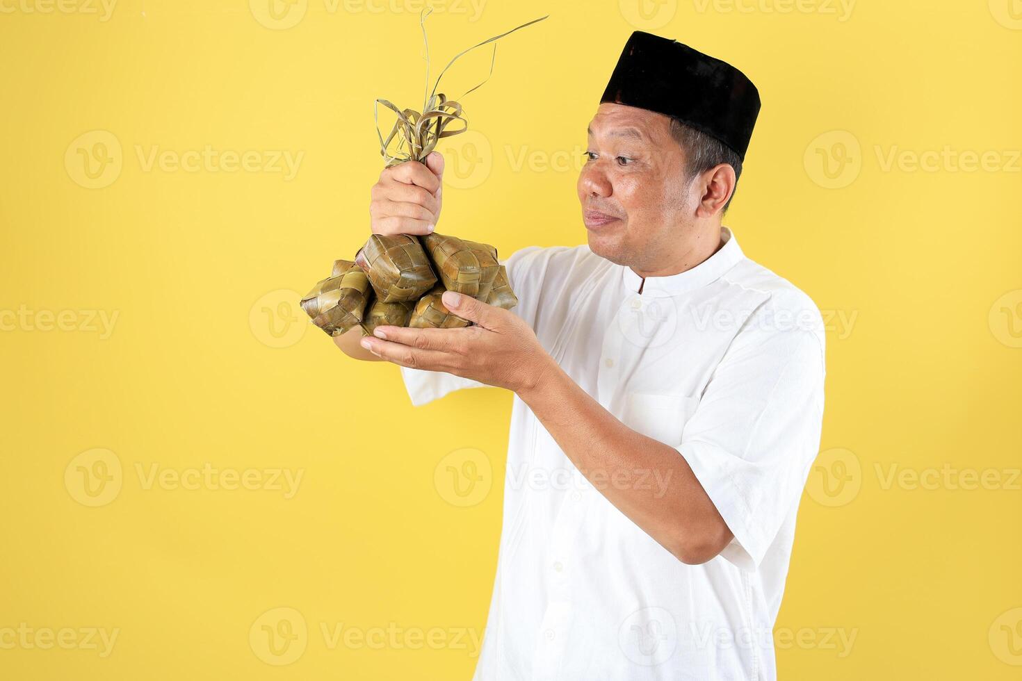 Asian Middle Age Man Wearing White Shirt Baju Koko and Black Caps Kopyah Holding Ketupat Rice Cakes for Eid al Fitr photo