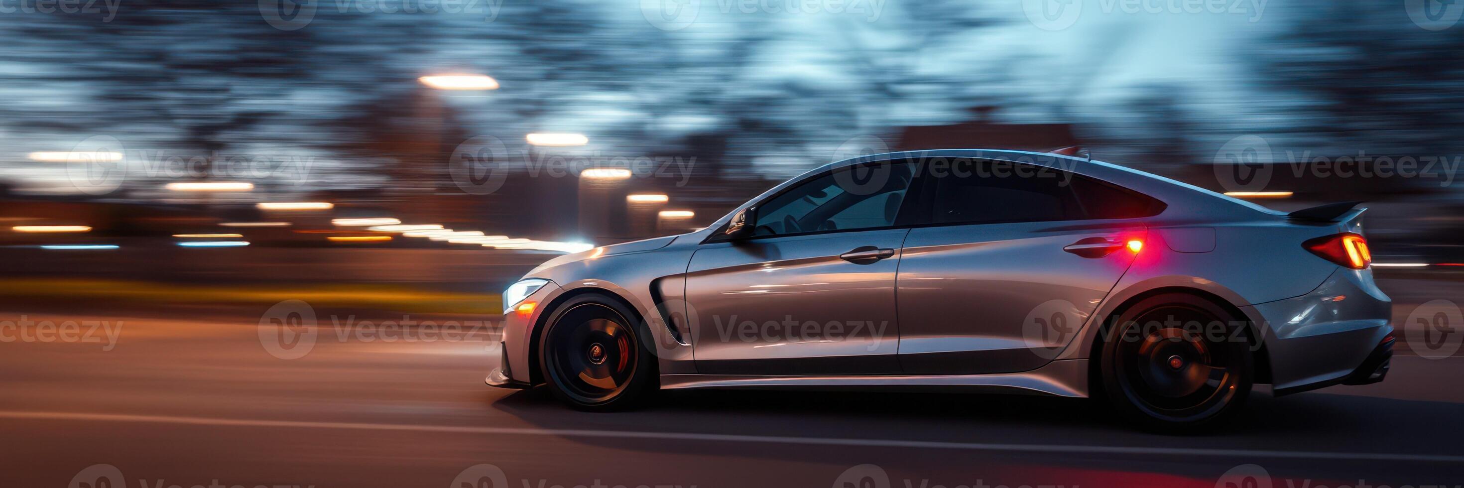 Sleek silver car speeding down a dimly lit street at twilight with motion blur effects photo