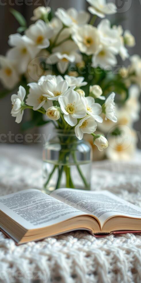 Open book placed on a table beside a vase of white flowers during the day photo