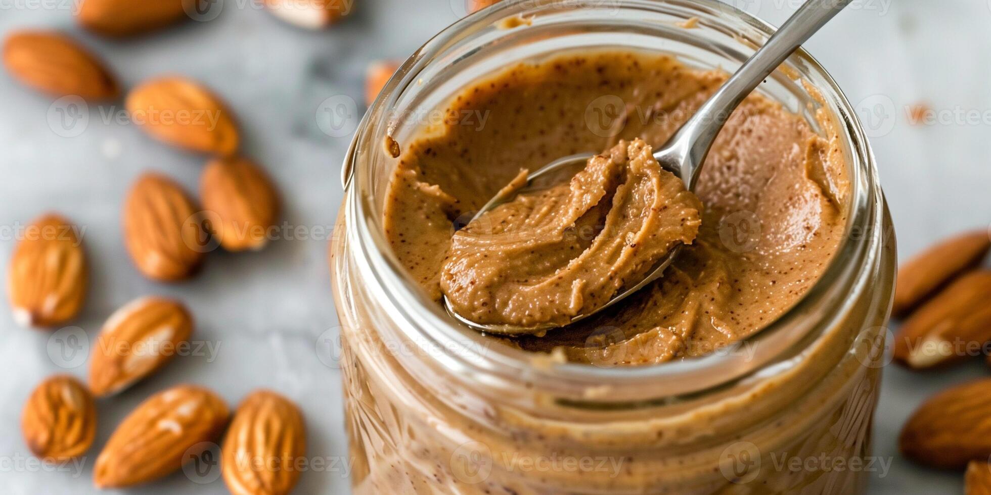 Glass jar of homemade almond butter with a spoon sticking out, surrounded by raw almonds, photorealistic photo