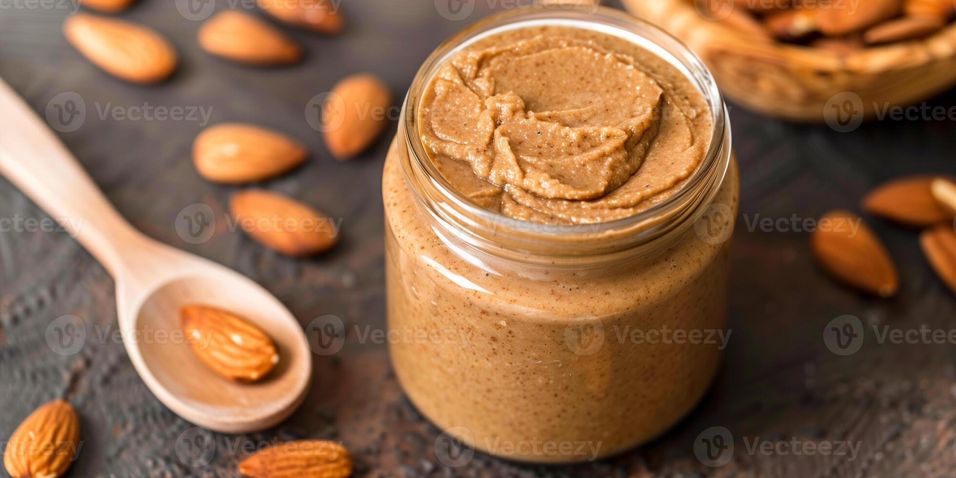 Jar of homemade creamy almond butter with wooden spoon and scattered almonds, picture photo