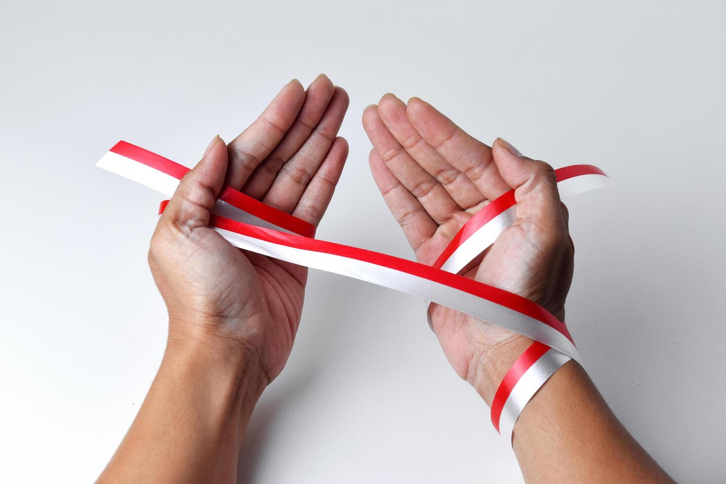 The hands of people praying are circled by a red and white ribbon photo