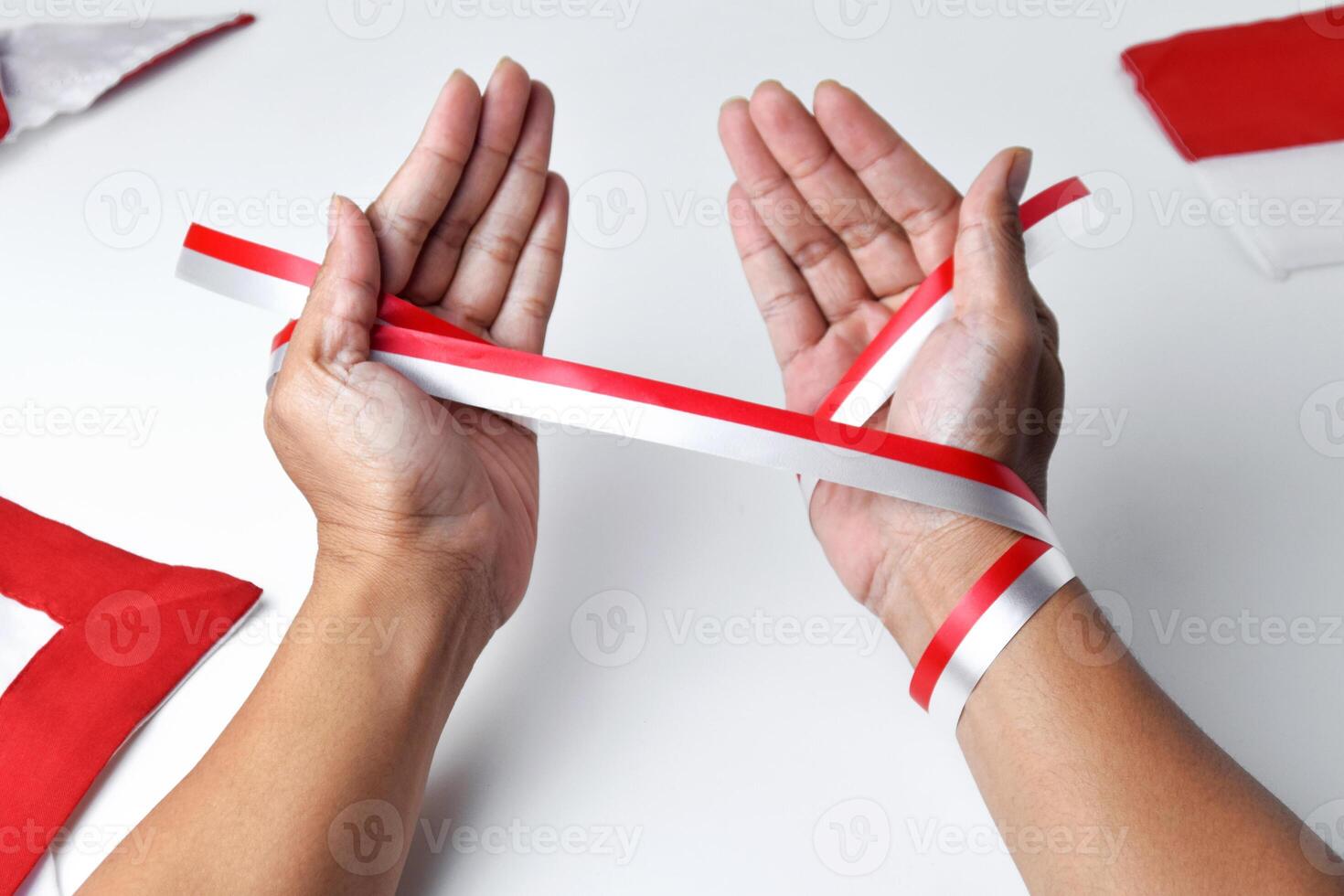 The hands of people praying are circled by a red and white ribbon photo