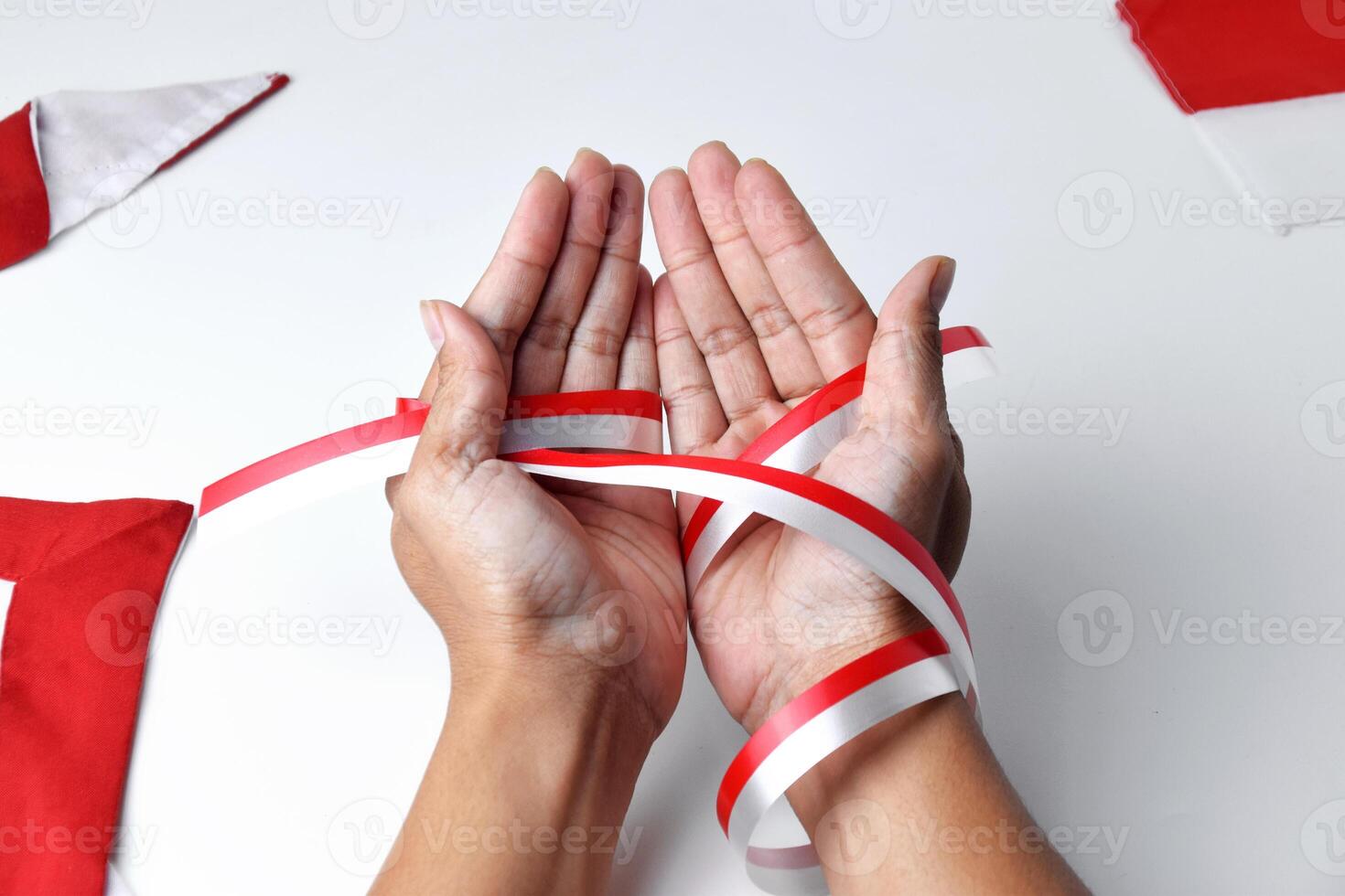 The hands of people praying are circled by a red and white ribbon photo