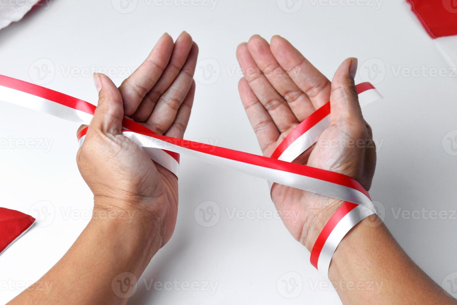 The hands of people praying are circled by a red and white ribbon photo