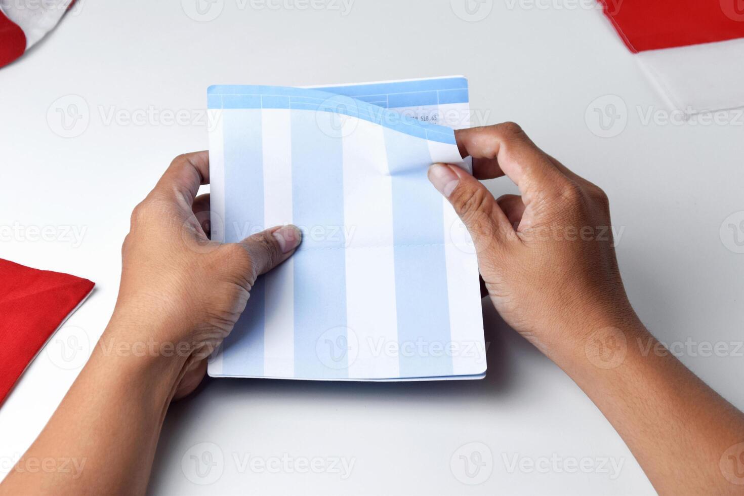 A person holds and opens a savings account book with a red and white background photo