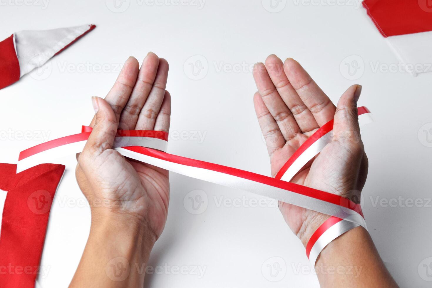The hands of people praying are circled by a red and white ribbon photo