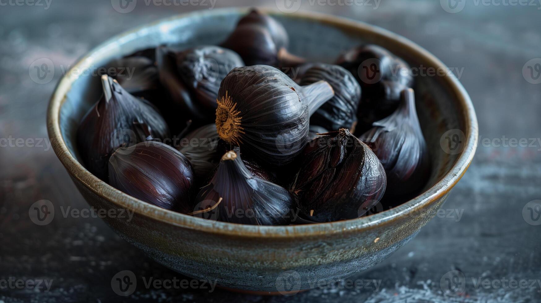 A small bowl filled with dark sweet fermented black garlic cloves ready to be used in cooking, photo