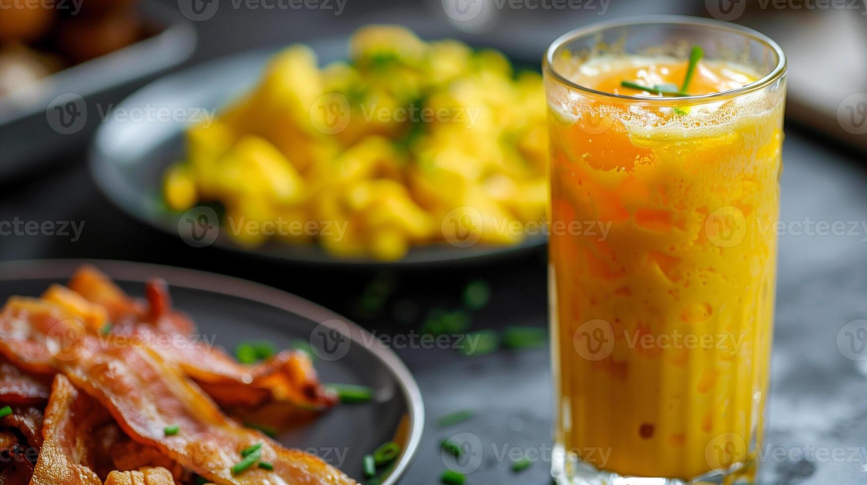 Tall glass of freshly squeezed orange juice beside a plate of scrambled eggs with chives and crispy bacon strips, photo