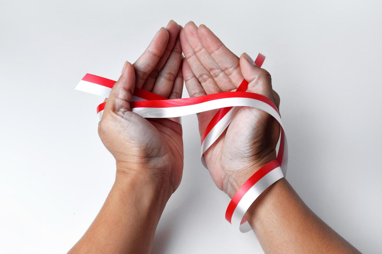The hands of people praying are circled by a red and white ribbon photo