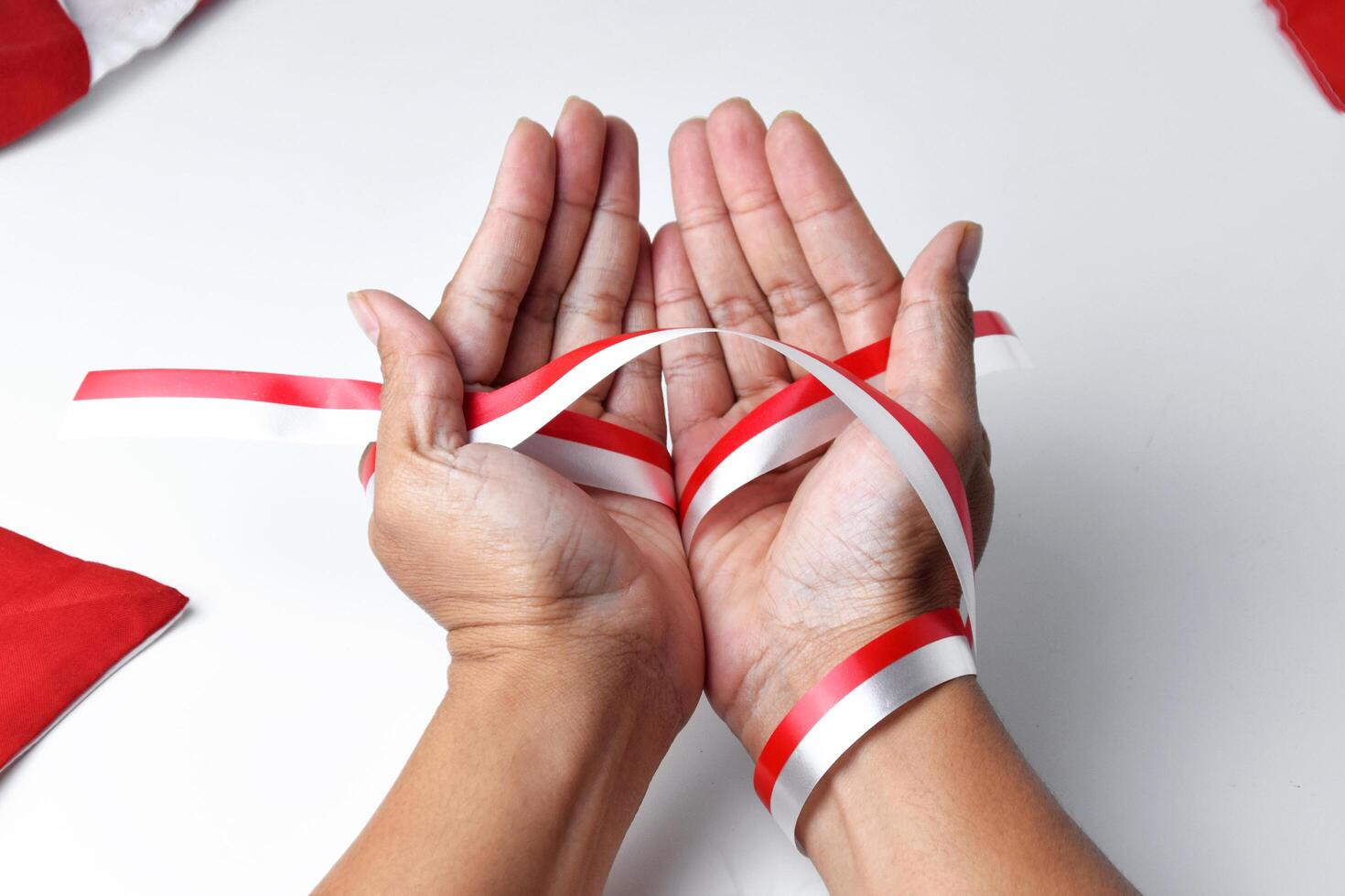 The hands of people praying are circled by a red and white ribbon photo