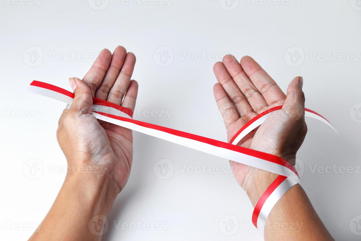 The hands of people praying are circled by a red and white ribbon photo