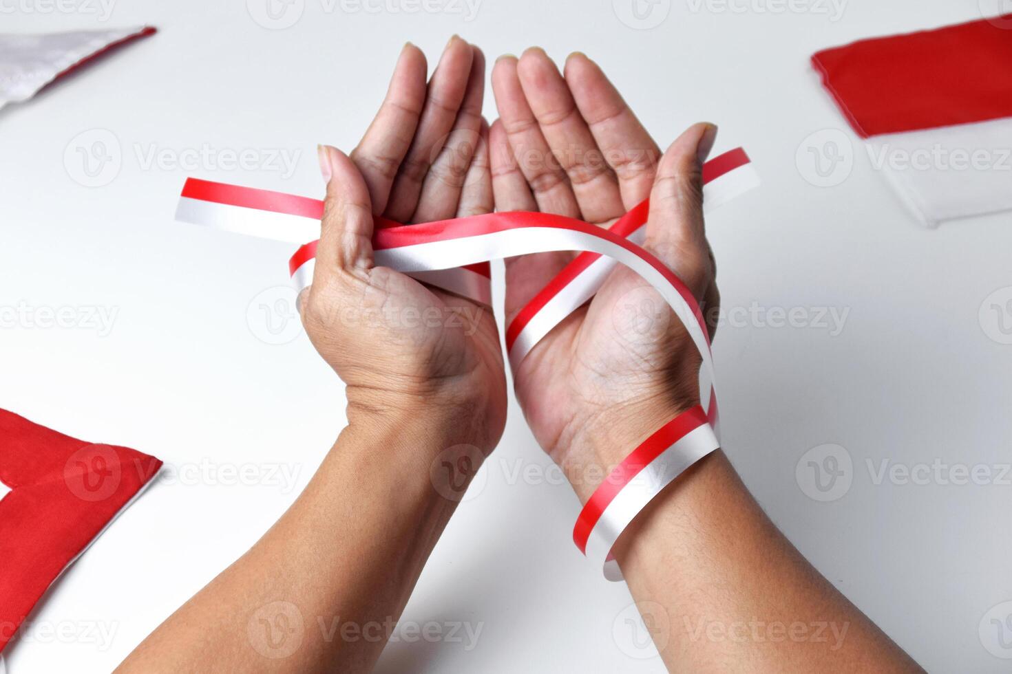 The hands of people praying are circled by a red and white ribbon photo