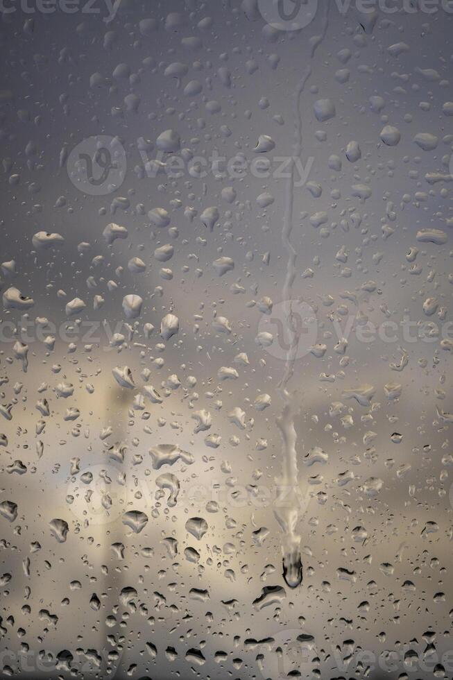 Rain drops on a window indicating gray and rainy day with defocused clouds and colors in background photo