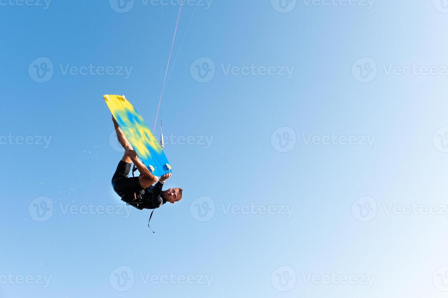 freestyle kiteboarding, freedom you can get. athlete hangs in the air during a trick on a kiteboard, on a clear blue sky photo