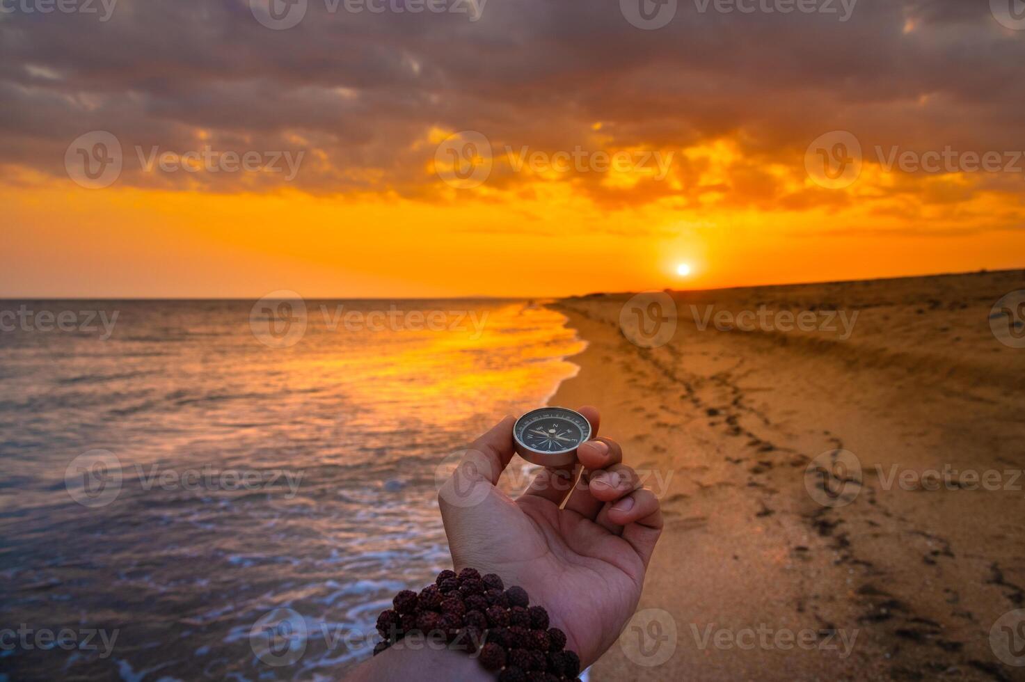 First person view of a man's hand holding a compass against a beautiful seascape. Navigation concept of finding your own way and orientation to the cardinal points photo