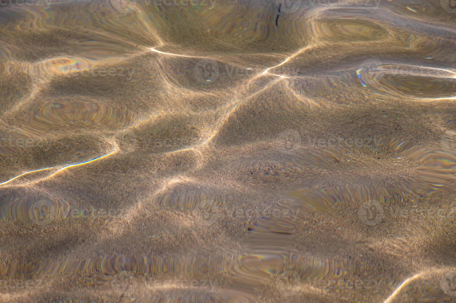 Through the transparent water of the ocean or sea you can see the sandy bottom with ridges of sand. Sun glare and ripples. View from above photo