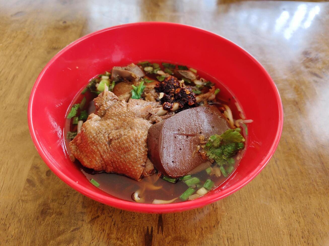 Braised duck noodles in bright red bowl on wood table. photo