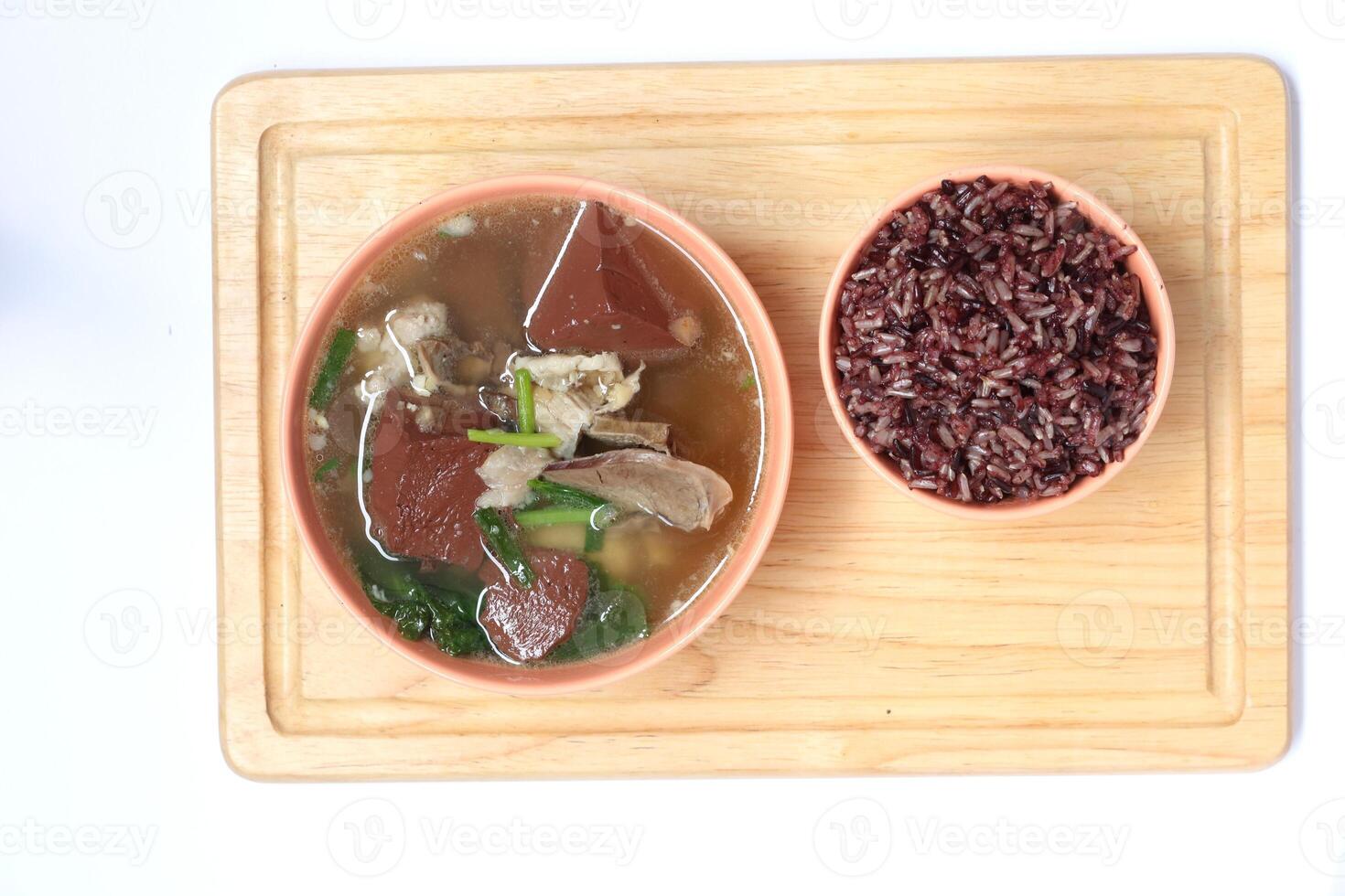 Pork blood jelly soup with entrials and riceberry rice in light orange ceramic bowl on light brown wood plate in top view. photo