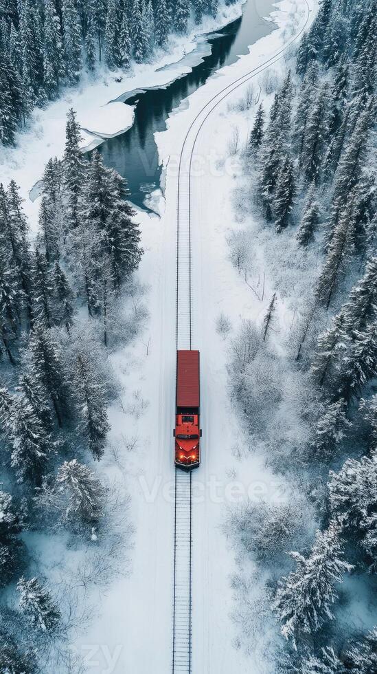 An aerial view of a red train traveling through a snowy forest photo