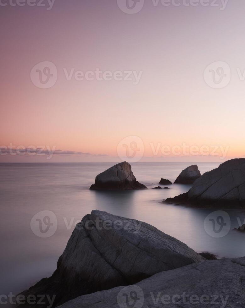 A long exposure photograph of rocks on the shore at sunset photo