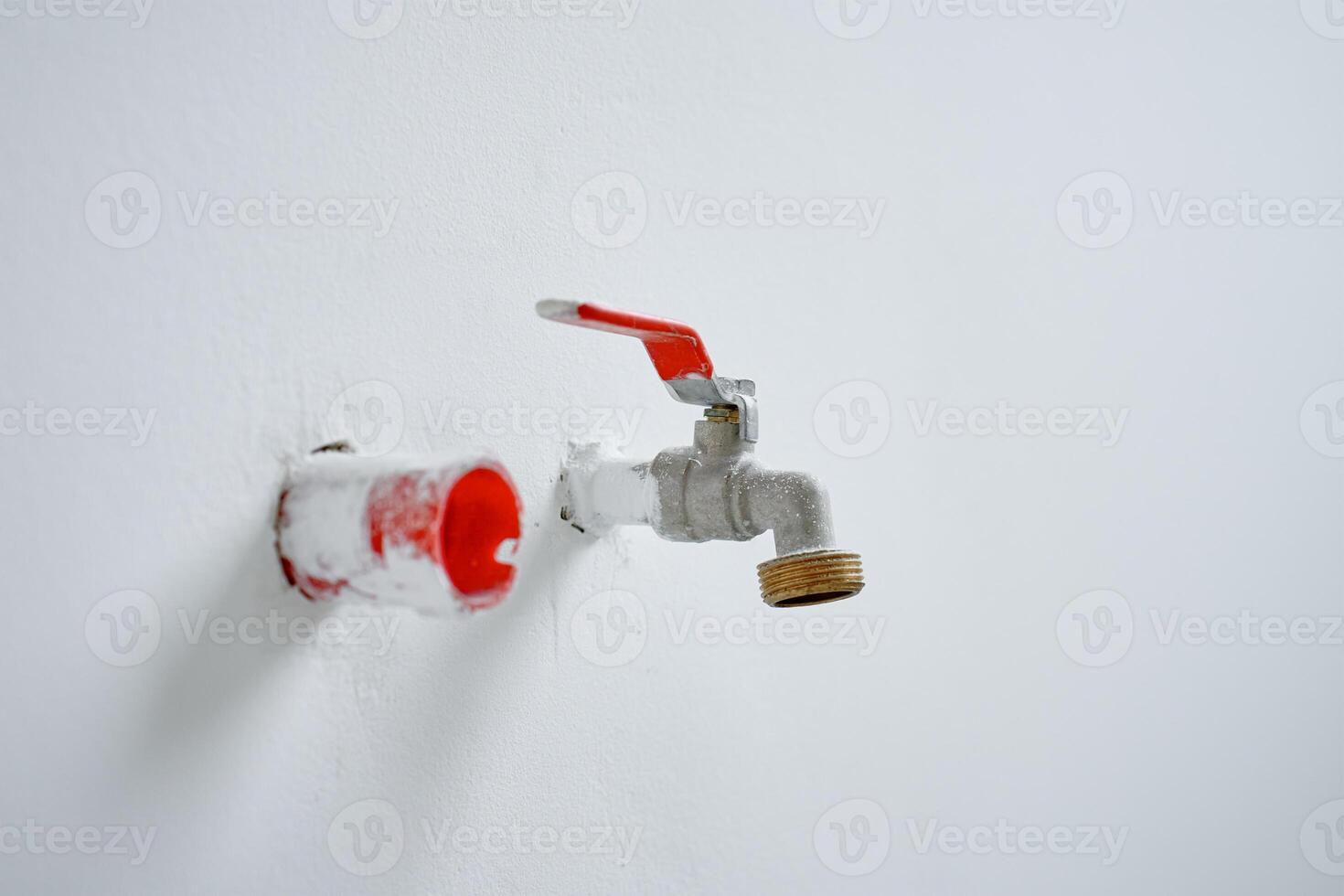 Water faucet with red handle protruding from white wall during home renovation photo