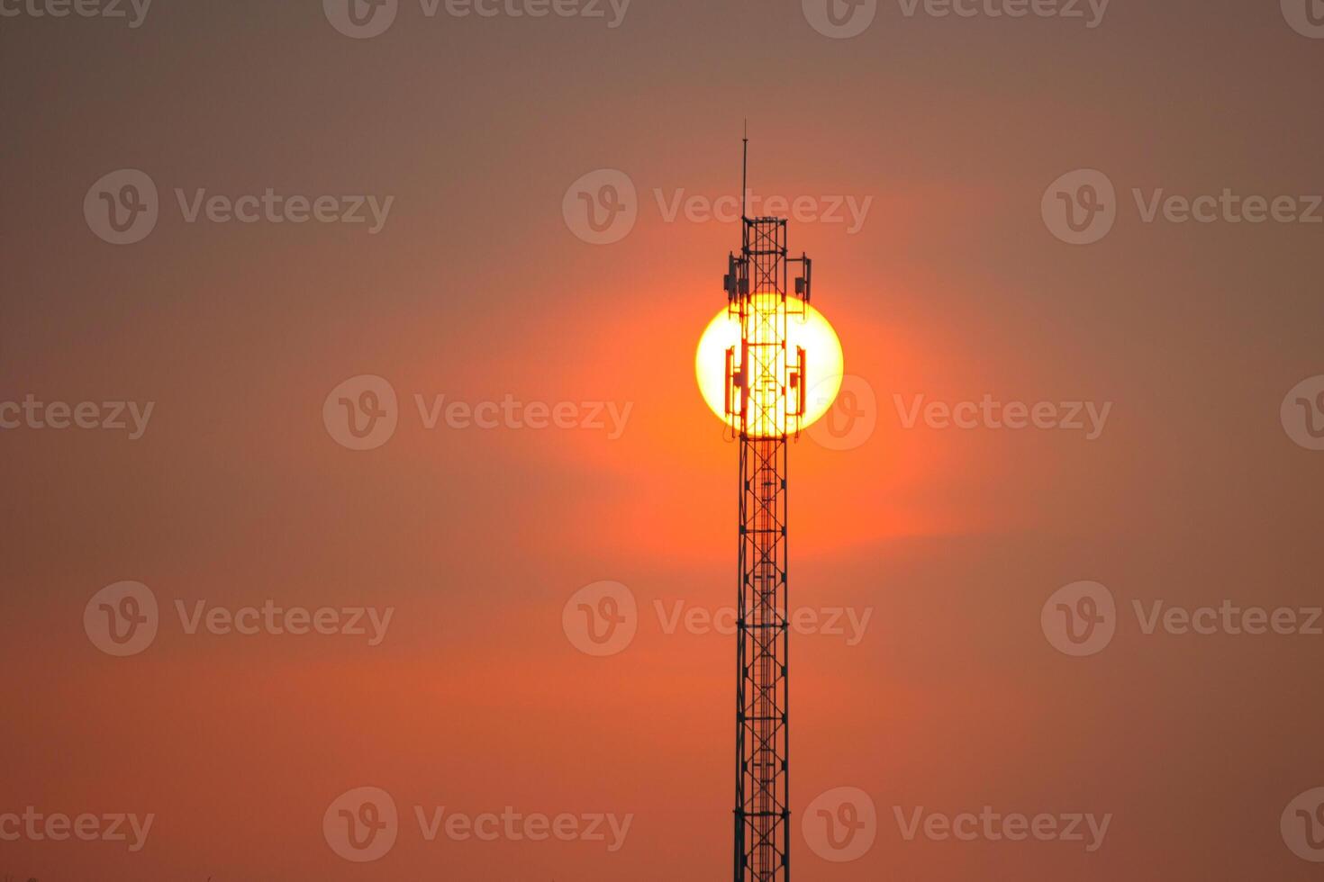 A cell tower with the sun setting behind it photo