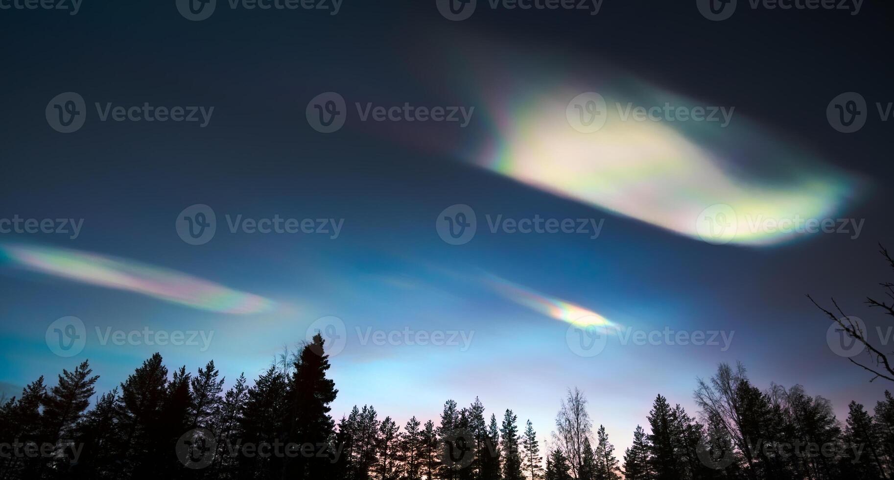 Nacreous clouds in dusk over tree silhouettes photo