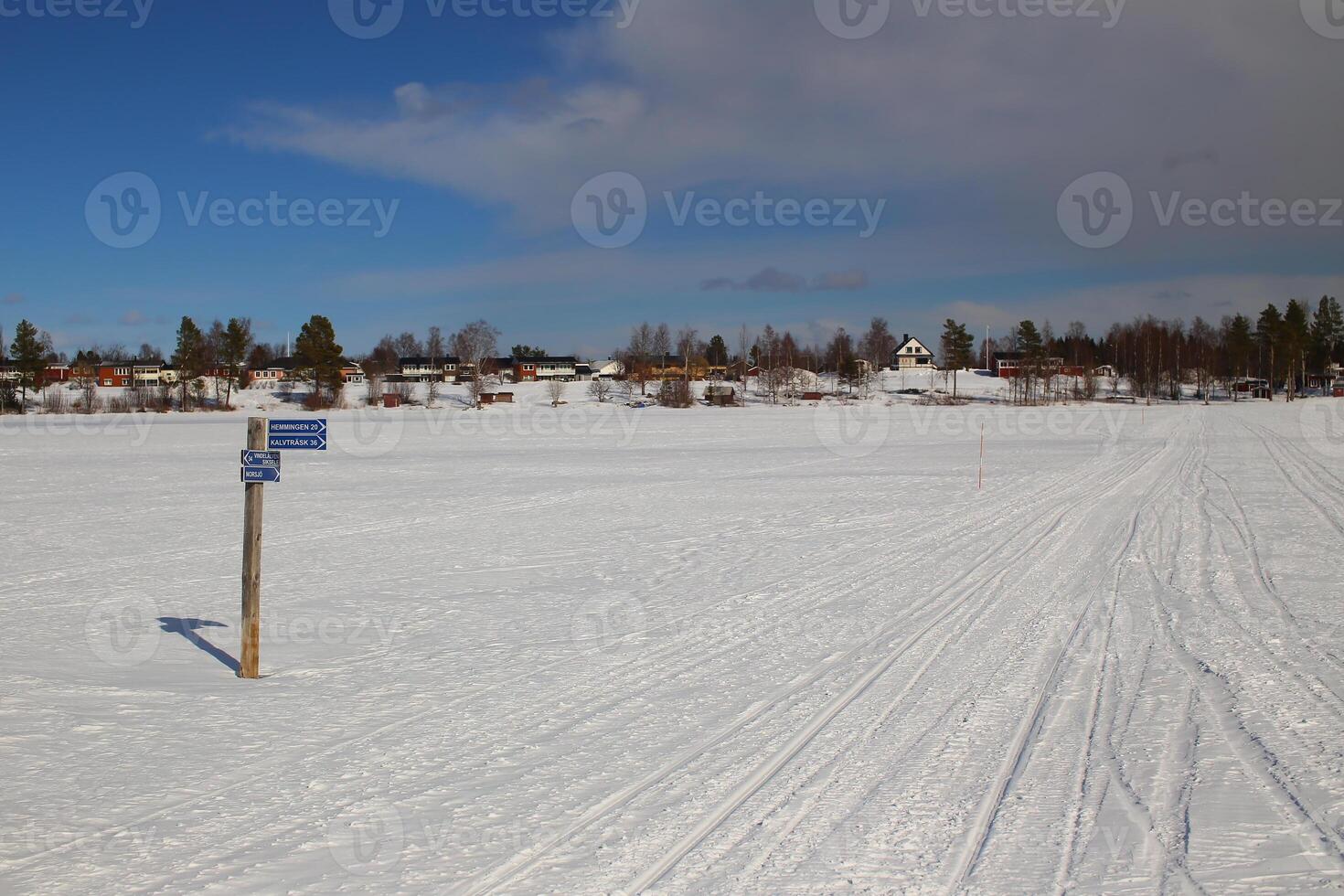 Signpost on frozen lake and the town Norsjo in Sweden. The signpost is pointing to Hamming, Kalvtrask, Vindelalven, Siksele and Norsjo photo